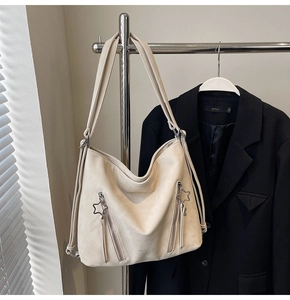 Detail of beige tote bag with star-shaped zipper pull and side pockets hanging on a suit