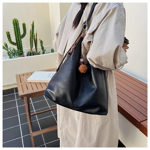 Detail of black pebbled leather tote bag with brown pompom and woven cord charm