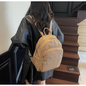 Detail of light brown lychee grain leather backpack with silver ring zippers and metal logo