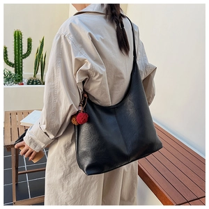 Detailed look at large black PU tote bag with fuzzy charm on model in beige coat