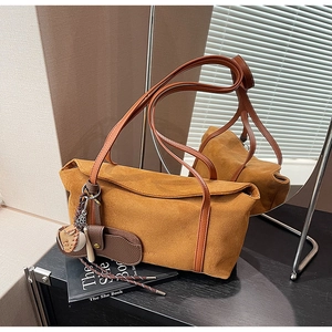 Détail macro d'un sac à bandoulière en daim caramel avec un charme de baseball et une sangle