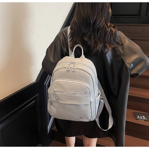 Detail of light grey pebbled leather backpack with silver zippers and multi-pocket design