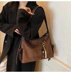 Close-up of brown vintage shoulder bag featuring metallic logo and stylish beaded charm