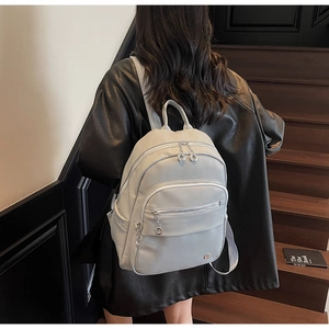 Close-up of light gray leather backpack with metallic zippers and silver charms on stairs