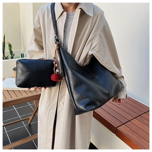 Detail of black leather bucket bag set with luxury pompom charm and matching clutch pouch