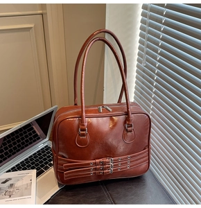 Detail of vintage brown leather tote bag with three belt buckle accents and laptop desk