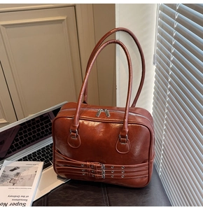 Detail of a brown glossy leather tote bag featuring parallel metal buckle straps