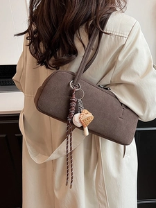 Dunkelbraune Retro-Schultertasche aus Wildleder mit gewebtem Anhänger auf beigem Trenchcoat