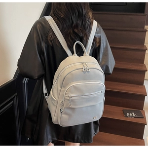 Close-up of a grey litchi grain faux leather backpack with silver metal zippers on back
