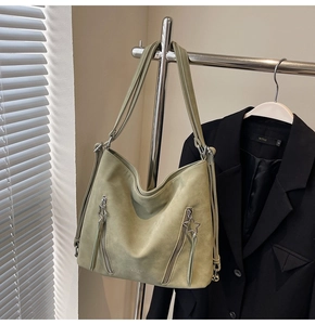 Close-up of sage green suede tote bag showing star metal zippers and front pockets