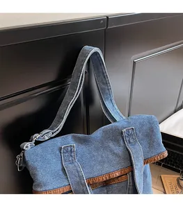Detail of adjustable strap and metal hooks on a blue denim tote with brown leather trim