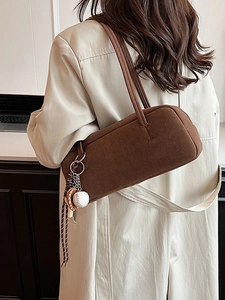 Retro dunkelbraune Wildleder-Achseltasche mit Baseball-Charm über einem beigen Mantel