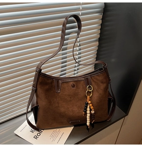 Detail of dark brown suede tote featuring contrast stitching and beaded tassel charm