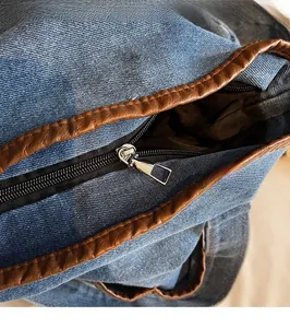 Detail view of the smooth silver zipper and brown leather trim on the denim bucket bag