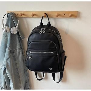 Close-up of black lychee grain leather backpack with silver zippers in a casual lifestyle setup