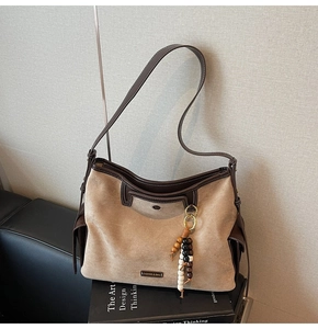 Detail of suede tote bag with contrast leather trim, stitching, and beaded tassel