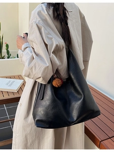 Large black hobo shoulder bag in soft leather with orange pompom on a model