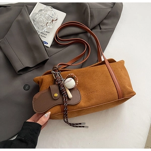 Caramel suede shoulder bag with vintage charms and brand embossing on white surface
