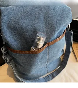 Detail of blue denim tote bag exterior pocket with brown trim holding a cosmetic bottle