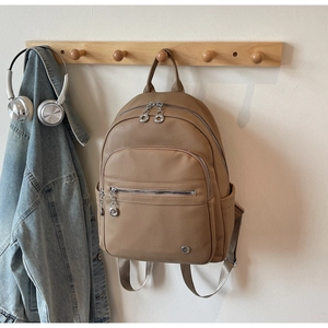 Detail view of khaki leather backpack with multi-layer zippers and silver hardware