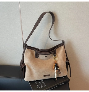 Close-up of large suede tote bag with beaded charm on a design book background