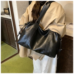 Close-up of a large black leather tote bag featuring reinforced stitching on wide straps