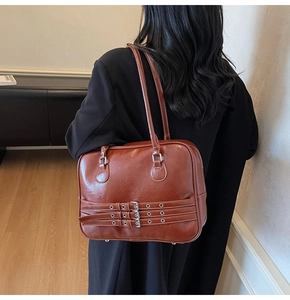 Detail of red-brown faux leather tote bag with three decorative silver buckle straps