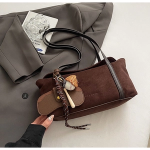 Dark brown suede tote bag with leather straps and baseball charm on a grey suit jacket