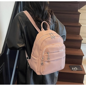 Pale pink lychee grain leather backpack shown on a model climbing dark wooden stairs
