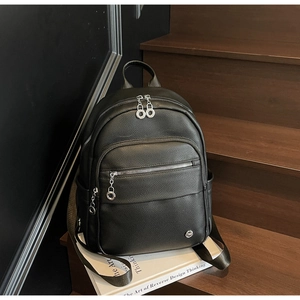 Close-up of black pebble grain leather backpack with silver zippers on a wooden step