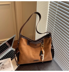 Detail of brown suede tote bag featuring a leather trim and a beaded wood charm
