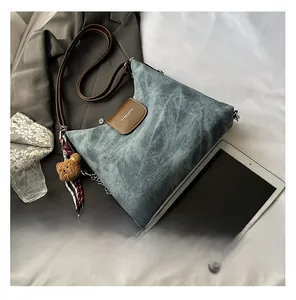 Détail du sac à bandoulière en denim bleu avec rabat en cuir brun et breloque ours
