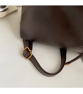 Close-up of the adjustable dark brown leather strap with a brass buckle on a bucket bag