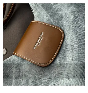 Macro d'un détail en cuir marron avec surpiqûres blanches sur un sac en jean denim