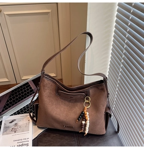 Detail of dark brown suede tote bag with boho beaded tassel and metal logo plate