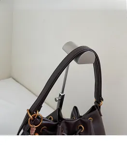 Detail view of deep brown bucket bag featuring gold metal buckles and leather drawstrings