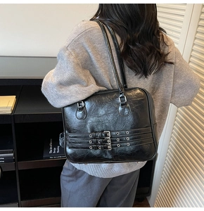 Detail of black vintage shoulder bag with metal eyelet straps and long handle design