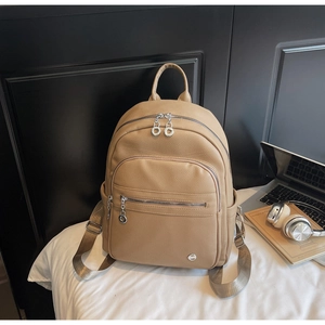 Close-up of khaki pebbled leather backpack showing multi-pocket design and silver hardware