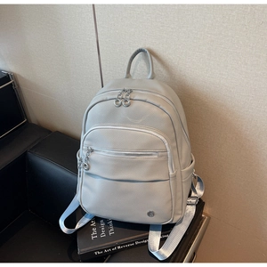 Detail of light gray pebbled leather backpack with silver zippers and blue woven straps