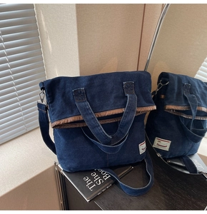 Detail view of denim tote bag with brown leather trim and adjustable shoulder strap