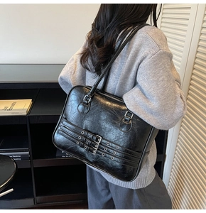 Detail of black glossy leather tote bag with triple buckle design worn by a model