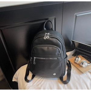 Detailed view of black litchi grain leather backpack with silver metal zippers on a bed