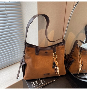 Close-up of brown suede tote bag with leather trim and colorful wooden bead tassel charm