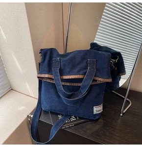 Detail showing the dark blue denim tote bag with brown leather trim and white woven label