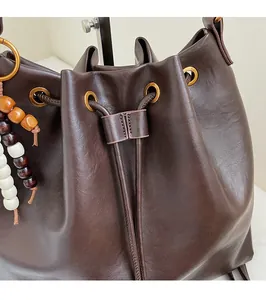 Detail view of coffee leather bucket bag with gold eyelets and colorful beaded tassel