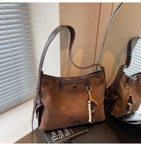Detail of brown suede tote bag with metallic logo, beaded tassel and adjustable strap