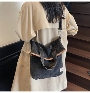 Black washed denim tote bag with leather trim shown on shoulder in a warm lifestyle setting