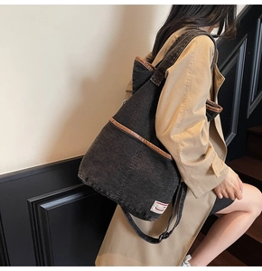 Detail of black denim tote bag featuring brown leather trim and white branded label