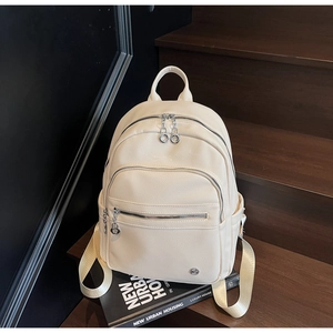Detail of off-white lychee texture leather backpack showing multi-zipper layers and straps
