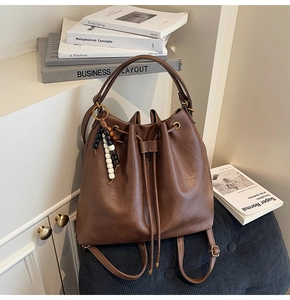 Detail of brown pleated bucket bag with beaded charm on a stool in home setting